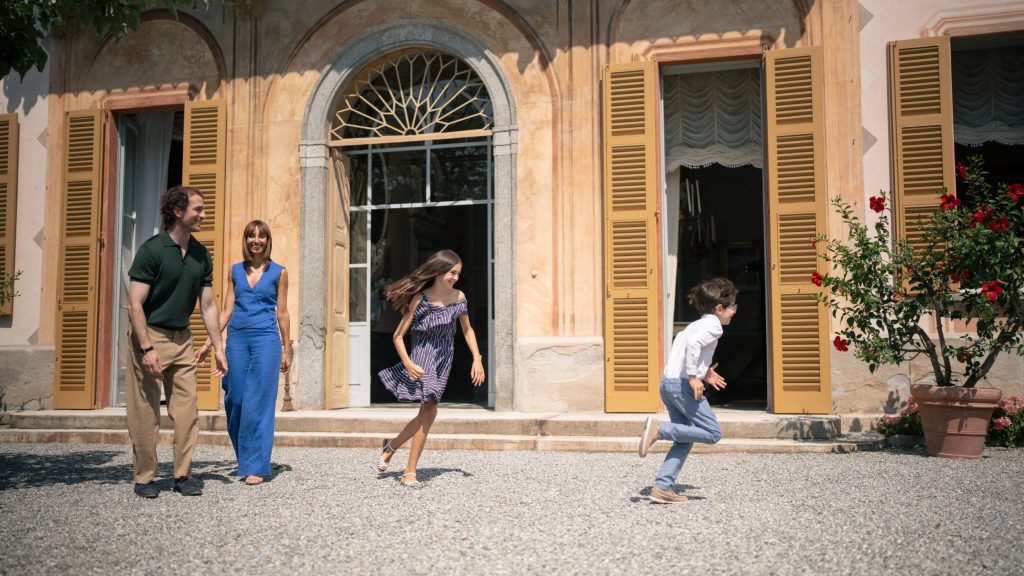Family walking outside a villa with open shutters and a flowering potted plant