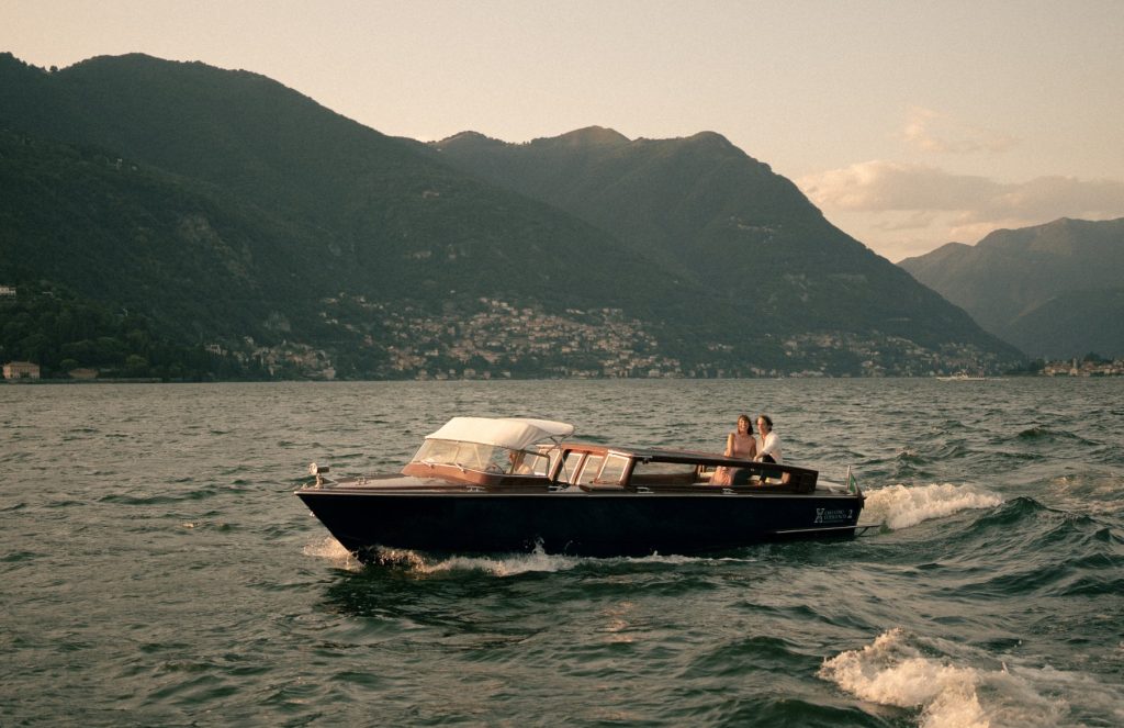 A motorboat with two people on Lake Como, with mountains in the background at sunset